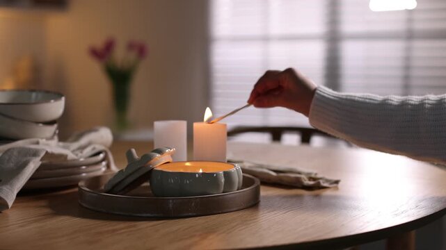Woman lighting up beautiful candles at dining table indoors, closeup