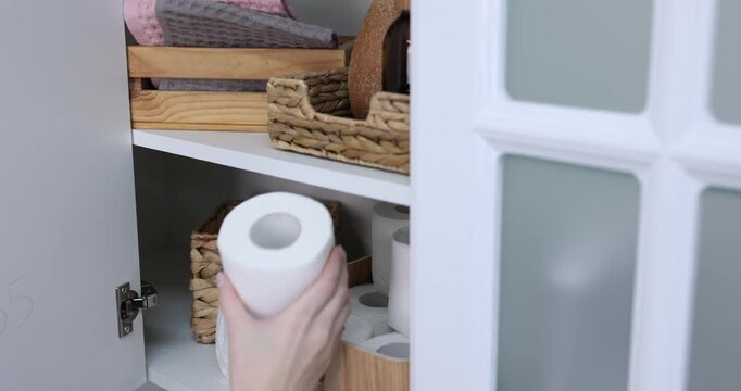 Woman putting toilet paper rolls into cabinet indoors, closeup