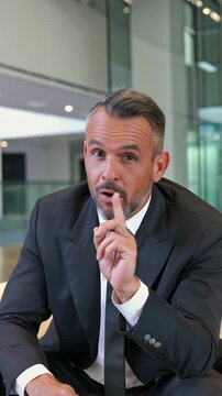 A mature businessman in a modern office lobby is shaking his finger and head, saying "No" to express disapproval, vertical shot
