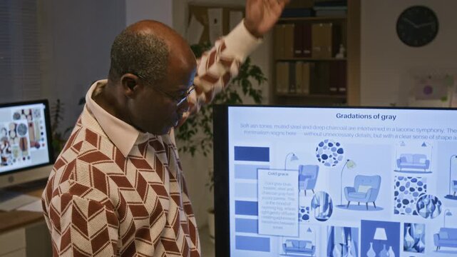 Senior African American man explaining design principles in home interior pointing at interactive screen while presenting to colleagues at office