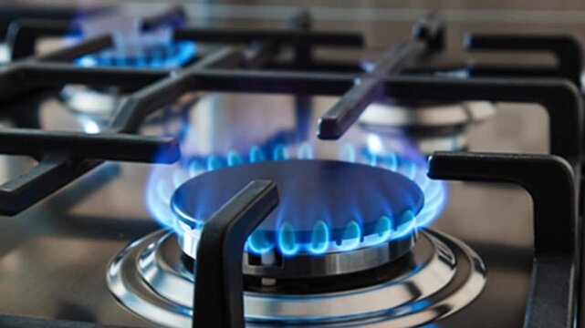 Close-up view of a modern gas stove burner with a bright blue flame ignited, ready for cooking in a kitchen setting.