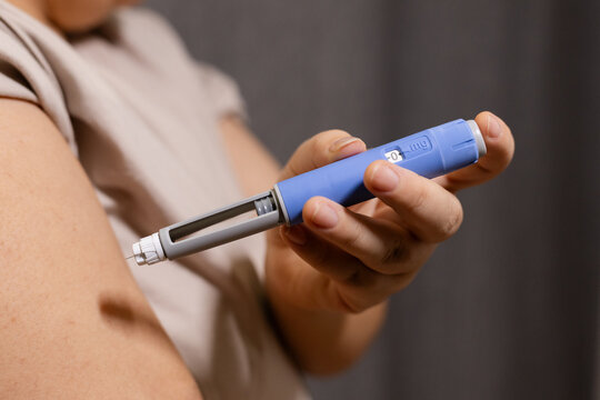 A horizontal close up of an young woman giving an injection to her shoulder