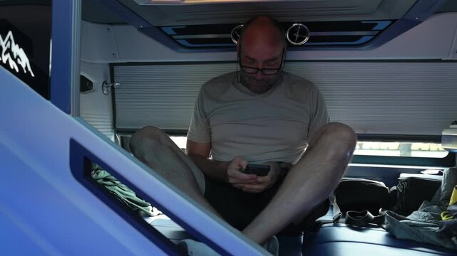Sleeper Bus Passenger Calmly Using Tablet In Vehicle. Person Seated Comfortably On Bus With Belongings Nearby. Passenger Engaged With Device In Personal Space Inside Bus Cabin With Vents