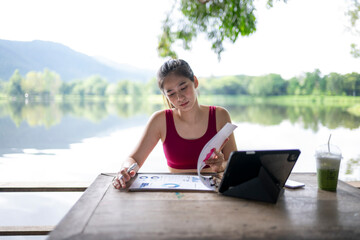 Fototapeta premium Woman working remotely outdoors by lake analyzing charts