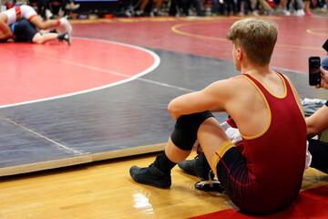 Young Man, a High School Wreslter is Sitting Nest to the Mat at a Wresting Tournament