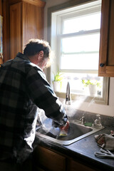 Man Washing Dishes in Kitchen by Bright Sunny Window