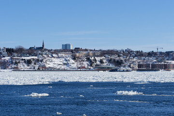 Obraz premium A winter view of Lévis from the port of Quebec City, featuring the Quai Paquet and ice on the St. Lawrence River.