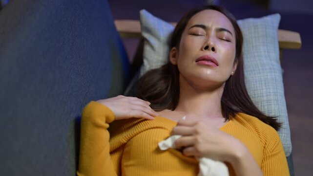 A woman is lying on a couch with a tissue in her mouth. She is in a yellow shirt and she is sick