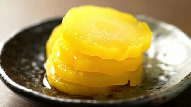 Stacked slices of bright yellow Takuan (Japanese pickled daikon radish) close-up on a rustic ceramic plate, an essential savory tsukemono side dish.