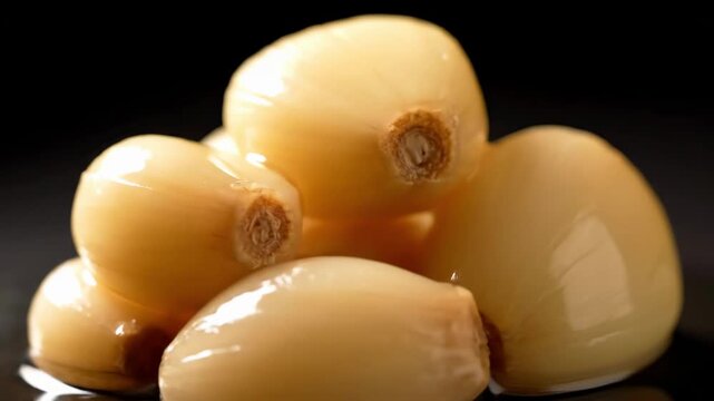 Macro shot of preserved peeled garlic cloves piled up, highlighting the smooth texture and glaze against a deep black background for culinary themes.