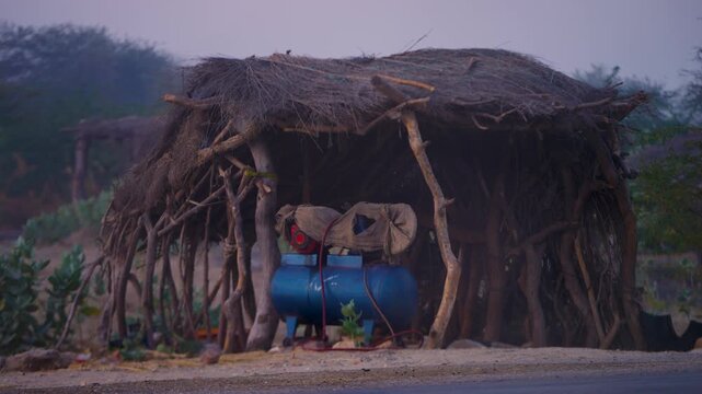 Rural Shelter With Blue Water Tank In Tharparkar Sindh Pakistan A Traditional Hut Constructed From Branches And Straw In A Desert Landscape.
