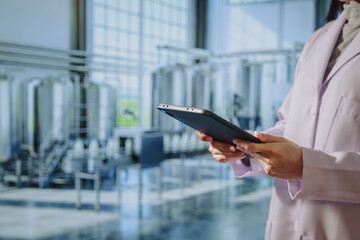 Asian young female quality control specialist holding a tablet in a modern dairy factory, approving production standards, ensuring food safety,hygiene compliance,smart manufacturing, industrial © Thitaporn