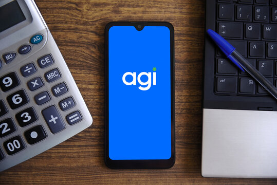 The Agibank (Agi) logo is displayed on a smartphone screen on a table with a calculator and notebook. The Brazilian bank Agibank raises US$276 million in its IPO in the US.
