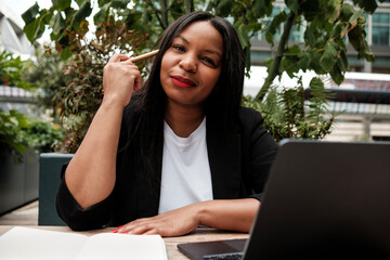 Businesswoman thinking and working with laptop and notebook in outdoor cafe