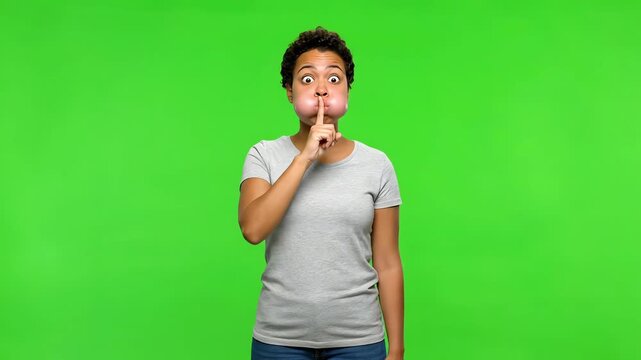 An expressive woman performs the shushing emoji action with puffed cheeks against a vibrant green screen.