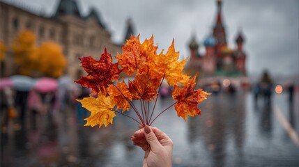 A beautiful woman's slender hand holds a bouquet of colorful maple leaves, with autumn in Moscow as background
