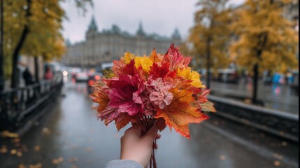 A beautiful woman's slender hand holds a bouquet of colorful maple leaves, with autumn in Moscow as background
