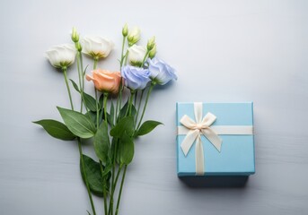 A bouquet of colorful flowers next to a small blue gift box on a light gray background with a white ribbon