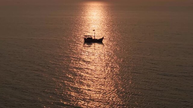 cinematic silhouette of a traditional fishing boat floating in the center of a golden sunpath