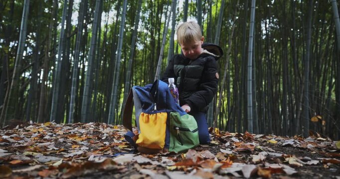 Little boy in bamboo thicket putting his juice back in his backpack - low shot