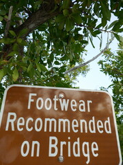 Footwear recommended on bridge sign with tropical plants in background vertical photo