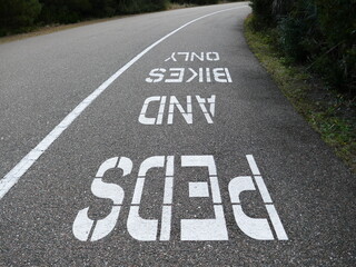 Fototapeta premium Peds and bikes only sign painted on asphalt path upside down departing view
