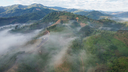 Fototapeta premium Aerial view of the rural village and dirt road in the mountains on foggy morning by drone