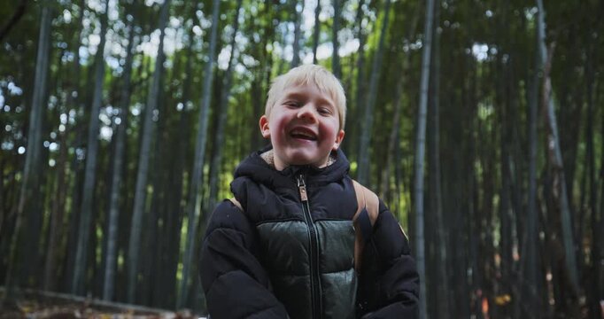Cute little blond boy dancing for camera in front of bamboo grove