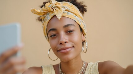 Beautiful young black woman taking a selfie portrait against a plain background wearing a yellow headband.