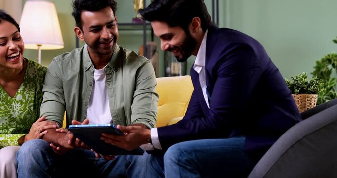 Indian couple discussing with agent at home with tablet computer during financial investment meeting with bank representative reviewing documents while sitting on sofa in cozy modern living room inter