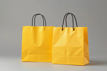 Two bright yellow paper shopping bags with black handles on grey background.