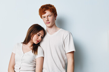 Naklejka premium Young couple standing close together on white background. Woman leaning head on man shoulder with casual white t shirts. Friendship, relationship and affection concept with studio portrait.