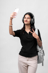 Naklejka premium young indian college girl with backpack and headphone taking selfie with smartphone
