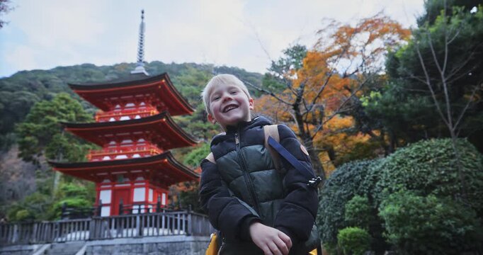 Smiling little boy in front of ancient Japanese tower playing rock, paper, scissors 
