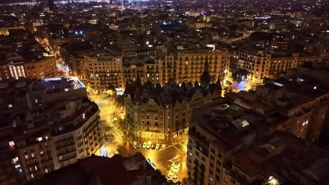 Illuminated Casa de les Punxes, famous landmark and cityscape at night, Barcelona in Spain. Aerial drone forward