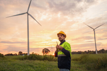 man in a yellow and black safety vest stands in front of two wind turbines