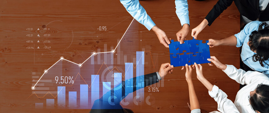 A diverse group of professionals collaborates on a business strategy, assembling a blue puzzle piece while analyzing charts and graphs on a wooden desk. Scalp