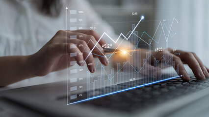 A close-up of hands typing on a laptop with an overlay of digital financial graphs and metrics,...