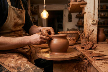 Mature Male Potter Shaping Clay on Pottery Wheel in Studio, Warm Lighting