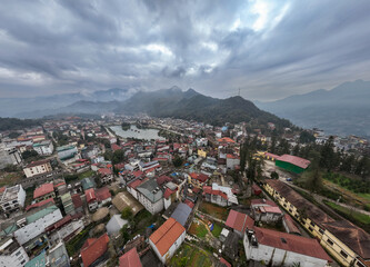 Obraz premium Aerial view of Sa Pa town in Vietnam, showcasing its scenic lake and surrounding misty mountains under a cloudy sky. A popular tourist destination.