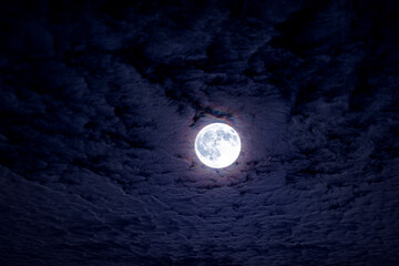 Fototapeta premium Bright full moon with dramatic night clouds. Moonlight on dark cloudy sky. Full moon in deep blue night atmosphere. Mystical lunar moon with clouds. Romantic night sky with shining full moon.
