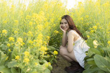 Fototapeta premium Happy young Asian woman smiling in beautiful yellow flower field. lovely lady in white dress enjoys serene outdoor summer day feeling joy and freedom