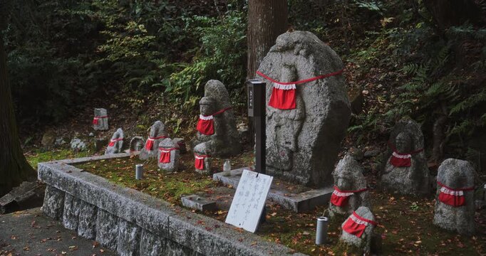 Ancient Japanese stone statues with red cloth on them in village - steady cam medium shot
