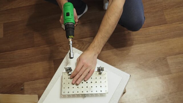 Caucasian man hands use cordless impact wrench to unscrew nuts on metal structure. Using cordless tool to disassemble homemade structures at home.