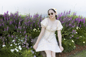 Happy beautiful woman smiling in floral fashion dress poses outdoor in purple flower garden. This cheerful lifestyle portrait shows carefree person enjoying summer