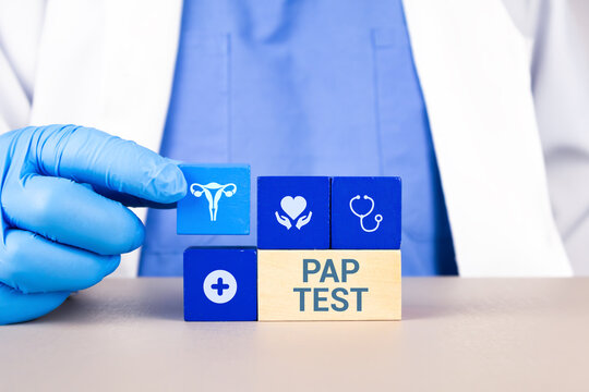 A gynecologist's hand arranges wooden cubes with a uterus icon. Concept of preventative information about the Pap smear, gynecological awareness, and early detection of uterine lesions.