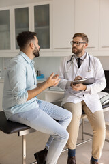 Fototapeta premium Medical anamnesis recording. Focused attentive doctor therapist hold clipboard pen listen to young male patient sharing complaints describing disease symptoms ask questions take notes in paper chart