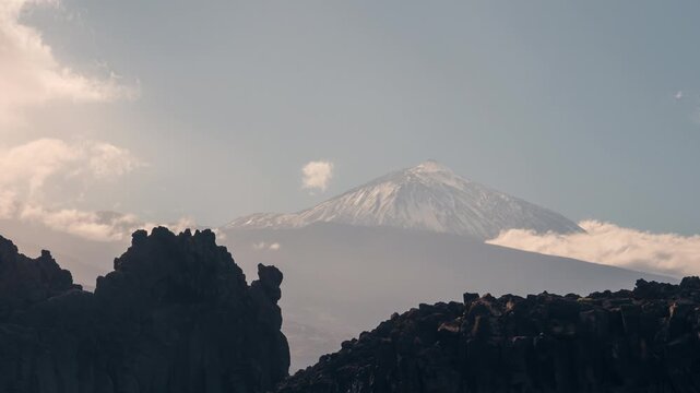 Sunny day timelapse at El Pris on Tenerife&rsquo;s north coast. Waves break against volcanic lava rocks while snow-capped Mount Teide rises in the background under moving clouds.