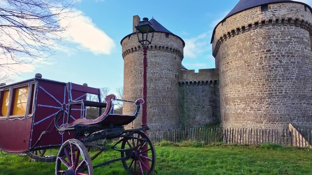 Vintage red horse-drawn carriage, or cal&egrave;che, parked on the grass in front of the stone walls of medieval Lassay castle in France
