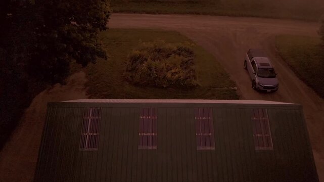 A rising drone shot of a house and truck in the countryside on an early morning.